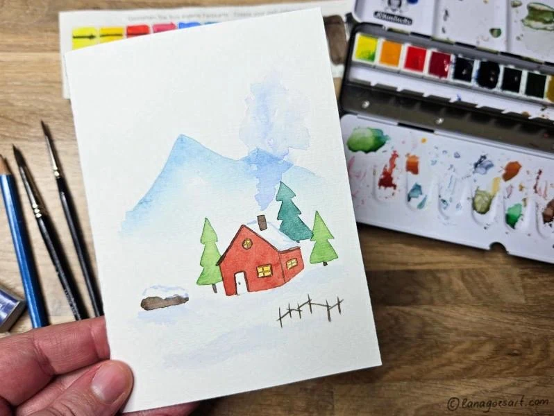 A Christmas card with a cute winter landscape, mountains, some trees and a red hut with paint supplies in the background.