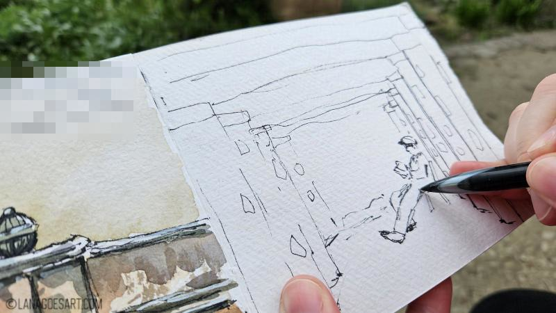 Open sketchbook with an ink sketch and a pen touching the page in the process.